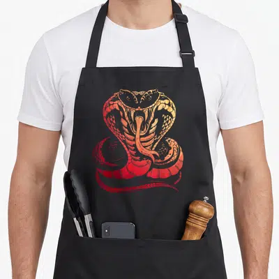 Cobra snake apron - Stylized snake coiled with mouth open facing forward in red orange yellow — shown on a black cotton canvas apron against a white background
