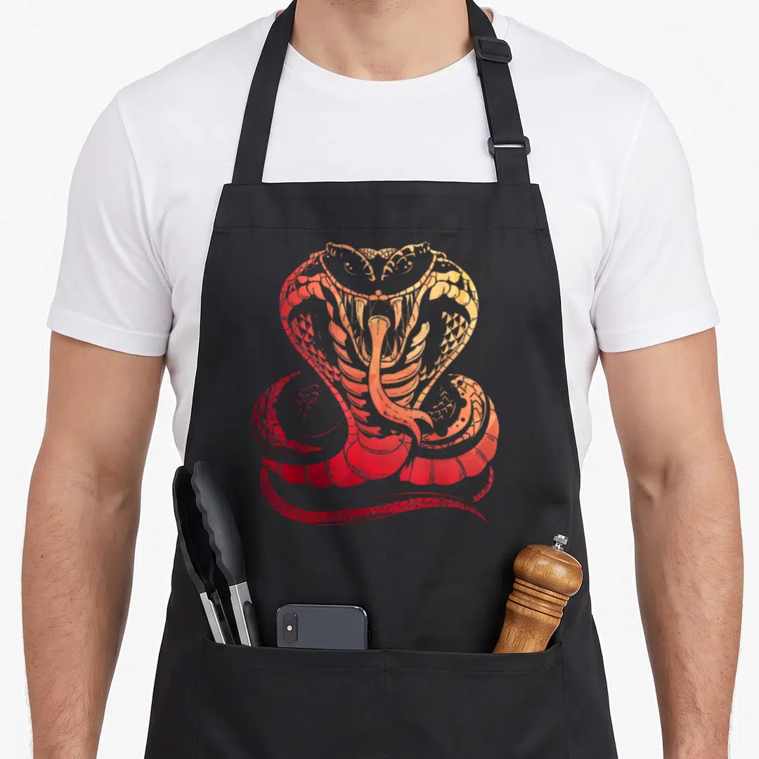 Cobra snake apron - Stylized snake coiled with mouth open facing forward in red orange yellow — shown on a black cotton canvas apron against a white background
