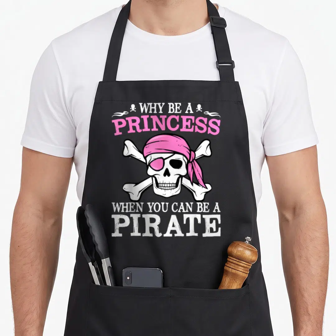 Funny pirate princess apron - Cartoon skull wearing pink bandana and eye patch with pirate slogan text — shown on a black cotton canvas apron against a white background