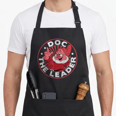 Leader snow white apron - Doc The Leader dwarf in red white circular border cartoon style — shown on a black cotton canvas apron against a white background