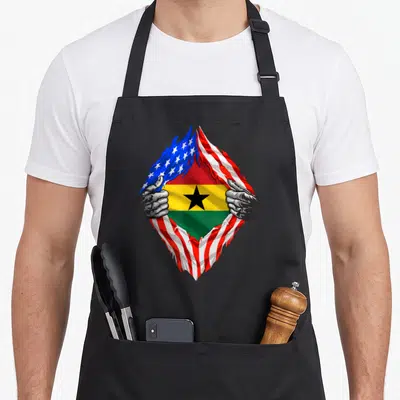 Ghana american flag apron - Torn US flag revealing Ghana flag held by grey hands — shown on a black cotton canvas apron against a white background
