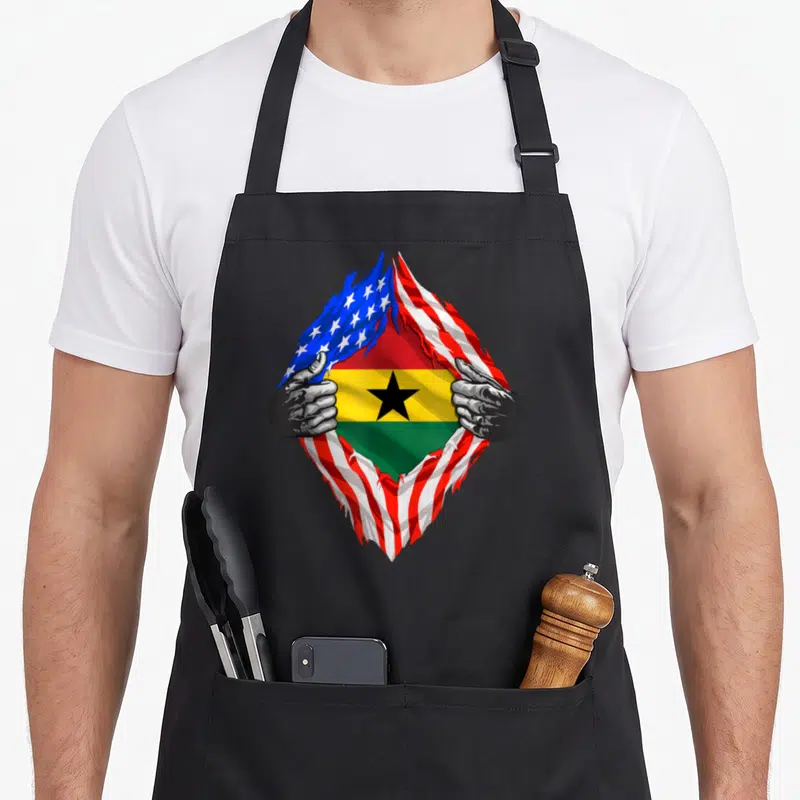 Ghana american flag apron - Torn US flag revealing Ghana flag held by grey hands — shown on a black cotton canvas apron against a white background