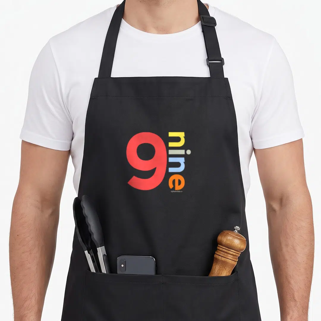 Nine age birthday apron - Large red nine with vertical multicolor lowercase n-i-n-e text on black fabric — shown on a black cotton canvas apron against a white background