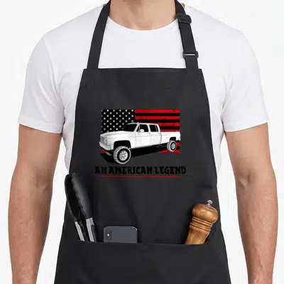Lifted muscle apron - White square body truck over red black flag with An American Legend text — shown on a black cotton canvas apron against a white background