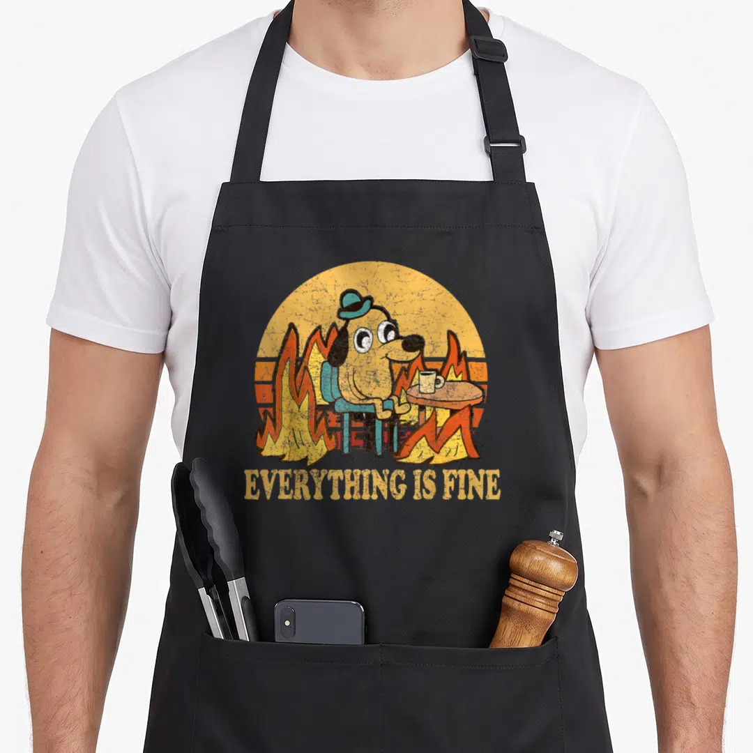 Fine dog apron - Cartoon dog in flames with mug and EVERYTHING IS FINE text — shown on a black cotton canvas apron against a white background