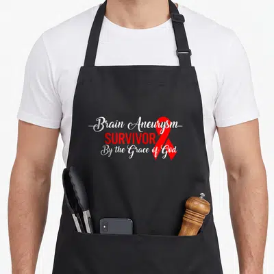 Brain aneurysm ribbon apron - Stacked white and red text reading Brain Aneurysm Survivor By the Grace of God with red — shown on a black cotton canvas apron against a white background