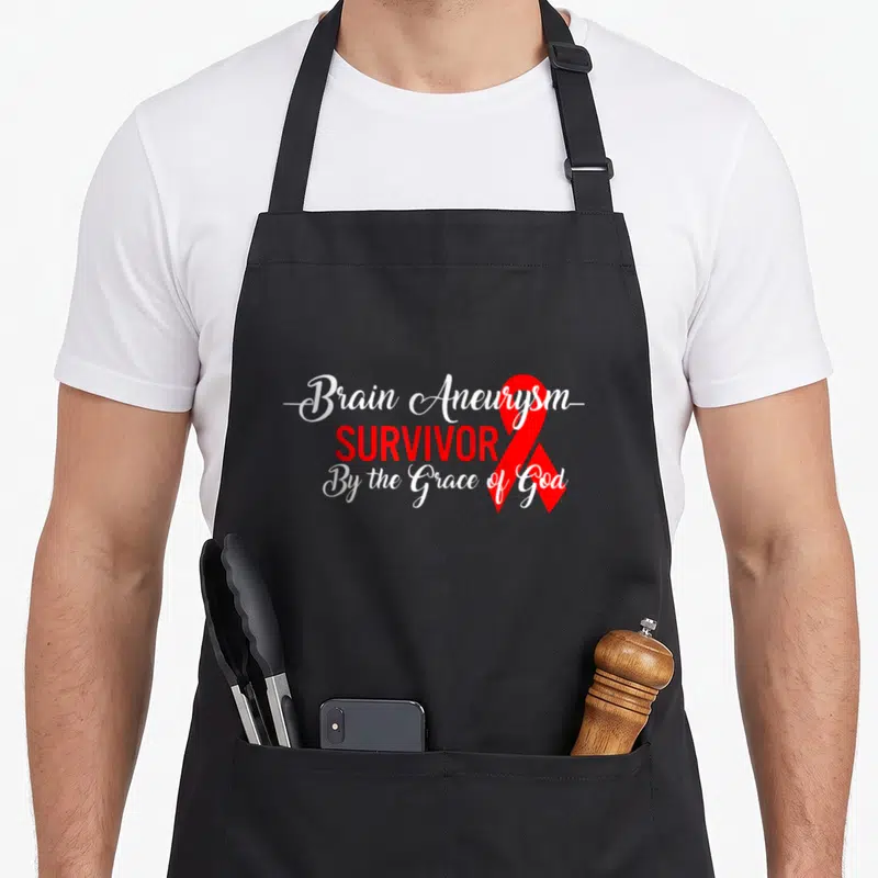 Brain aneurysm ribbon apron - Stacked white and red text reading Brain Aneurysm Survivor By the Grace of God with red — shown on a black cotton canvas apron against a white background