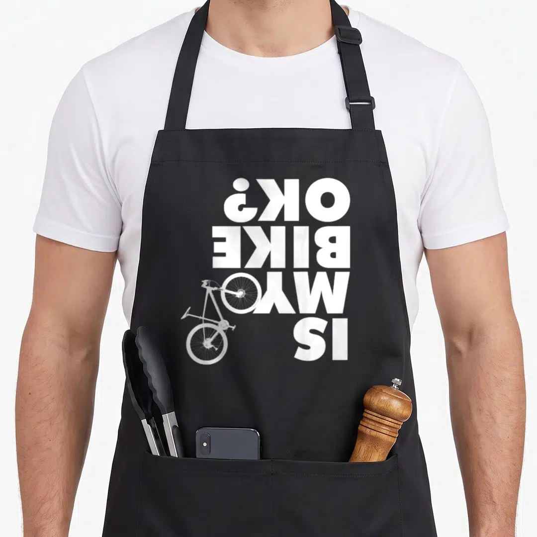 Funny bike apron - Upside down white text IS MY BIKE OK next to upright bicycle graphic — shown on a black cotton canvas apron against a white background