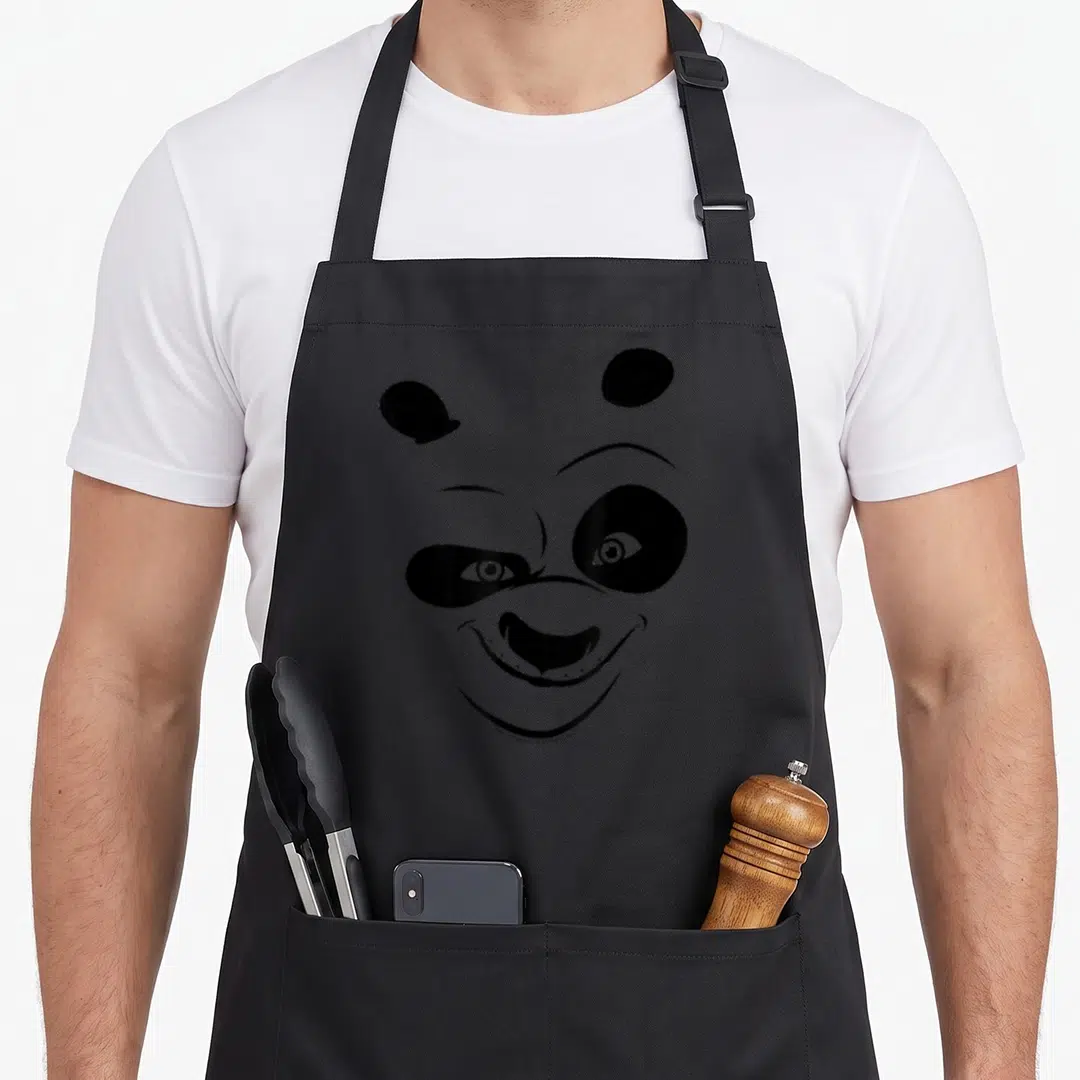 Kung face apron - Minimalist black panda face winking on grey background — shown on a black cotton canvas apron against a white background