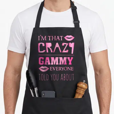 Gammy grandma apron - Pink stacked text I'M THAT CRAZY GAMMY with lip icons on black bib apron — shown on a black cotton canvas apron against a white background