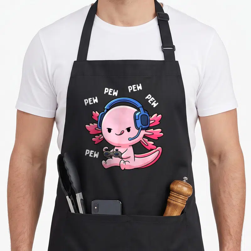 Pew video game apron - Pink axolotl with blue headphones holding grey controller surrounded by white PEW text — shown on a black cotton canvas apron against a white background