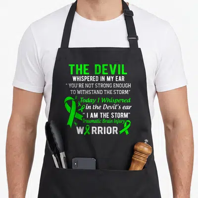 Storm tbi awareness apron - Green and white stacked text with one large and four small TBI awareness ribbons — shown on a black cotton canvas apron against a white background