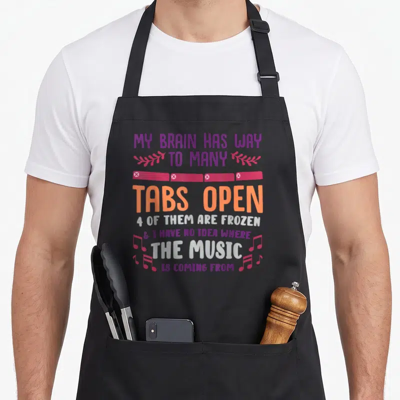 Many open apron - Stacked text about frozen tabs and music with pink banner and musical notes — shown on a black cotton canvas apron against a white background