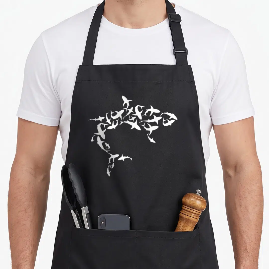 Shark science apron - White shark silhouette formed by many small shark shapes on grey background — shown on a black cotton canvas apron against a white background