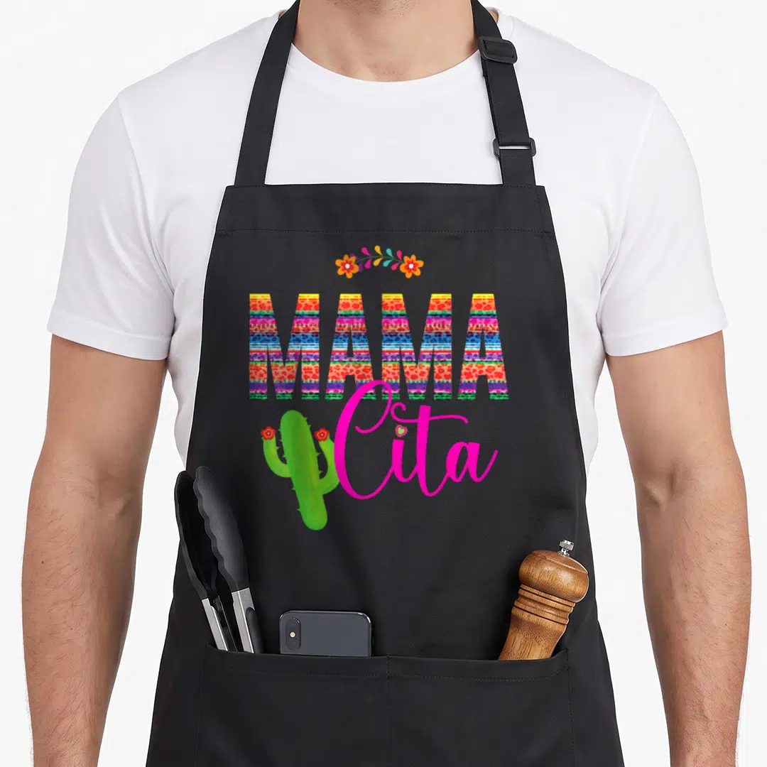 Mamacita cactus apron - Colorful MAMA cita text with striped patterns, floral arch, and green cactus illustration — shown on a black cotton canvas apron against a white background