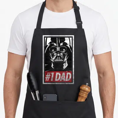 Propaganda falcon dad apron - Distressed Darth Vader face above red banner reading #1 DAD in white text within a white — shown on a black cotton canvas apron against a white background