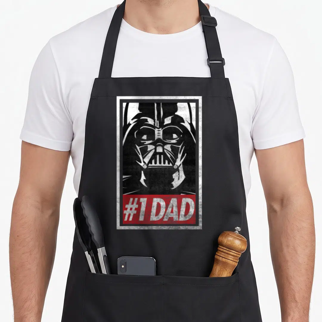 Propaganda falcon dad apron - Distressed Darth Vader face above red banner reading #1 DAD in white text within a white — shown on a black cotton canvas apron against a white background