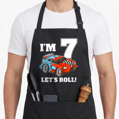 Seven car apron - Cartoon red and blue race car with I'M 7 LET'S ROLL! text — shown on a black cotton canvas apron against a white background