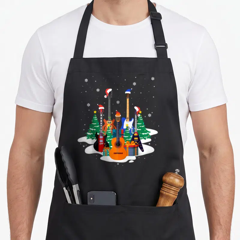 Guitar santa aprons - Five cartoon guitars with Santa hats among Christmas trees and presents in snow — shown on a black cotton canvas apron against a white background