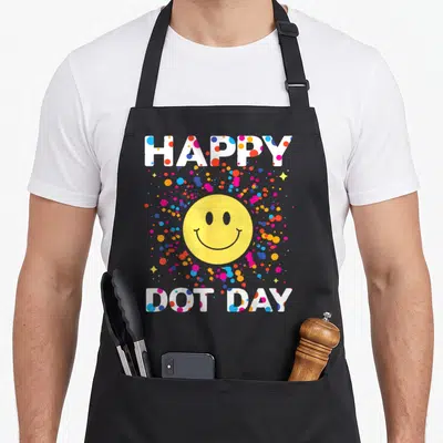 Colorful polka dot apron - HAPPY DOT DAY text with yellow smiley face and multicolored dots — shown on a black cotton canvas apron against a white background