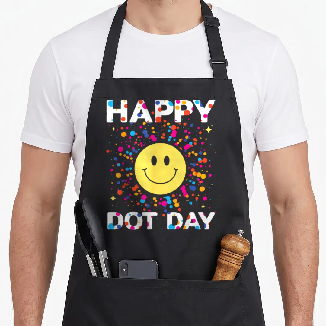Colorful polka dot apron - HAPPY DOT DAY text with yellow smiley face and multicolored dots — shown on a black cotton canvas apron against a white background