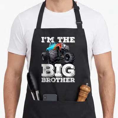 Brother truck apron - I'M THE BIG BROTHER text surrounding a blue and orange monster truck illustration — shown on a black cotton canvas apron against a white background