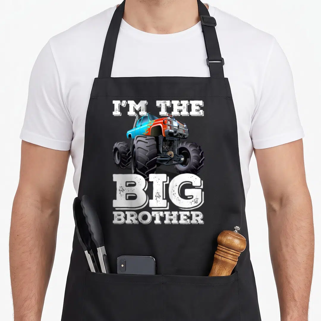 Brother truck apron - I'M THE BIG BROTHER text surrounding a blue and orange monster truck illustration — shown on a black cotton canvas apron against a white background