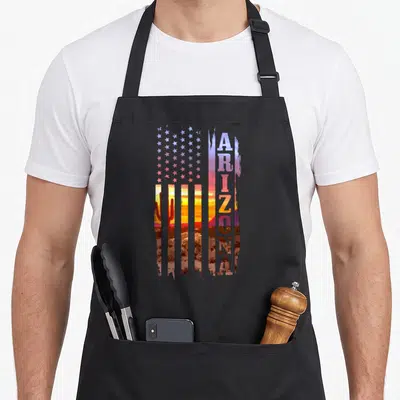 Landscape american flag apron - Stylized flag with Arizona sunset cactus and vertical text in purple orange brown — shown on a black cotton canvas apron against a white background