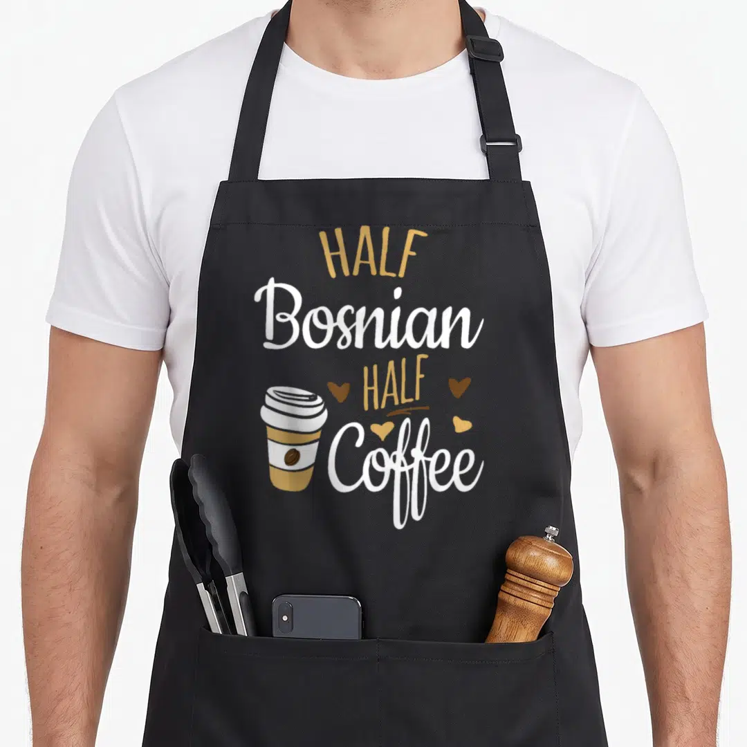 Bosnian coffee apron - Stacked text reading Half Bosnian Half Coffee next to a cartoon coffee cup and three scattered — shown on a black cotton canvas apron against a white background