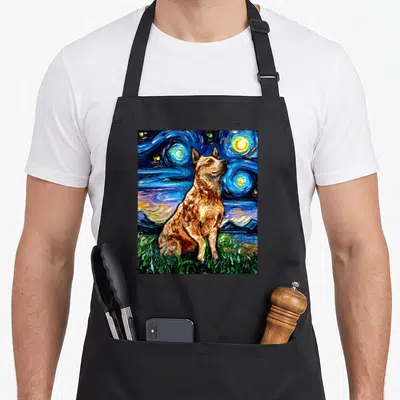 Heeler starry dog apron - Watercolor cattle dog sitting on green grass under a swirling blue night sky with yellow stars — shown on a black cotton canvas apron against a white background