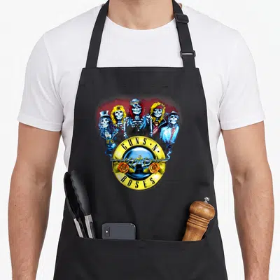 Gun skeleton apron - Five cartoon skeletons in a heart shape above a yellow Guns N Roses logo with guns and roses — shown on a black cotton canvas apron against a white background