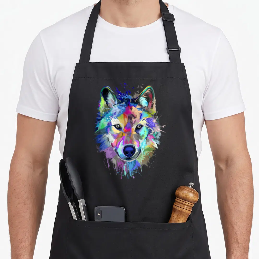 Wolf splash aprons - Multicolored watercolor wolf head with blue, purple, pink, yellow, and green paint splatter effects — shown on a black cotton canvas apron against a white background
