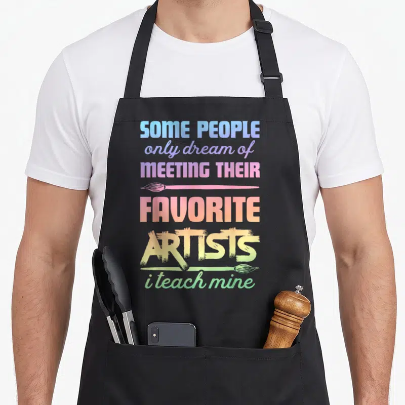 Teach painter apron - Stacked rainbow text with two horizontal paintbrushes and inspirational quote — shown on a black cotton canvas apron against a white background