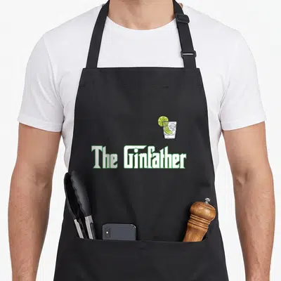 Ginfather gin apron - The Ginfather text with cartoon gin and tonic glass and lime slice — shown on a black cotton canvas apron against a white background