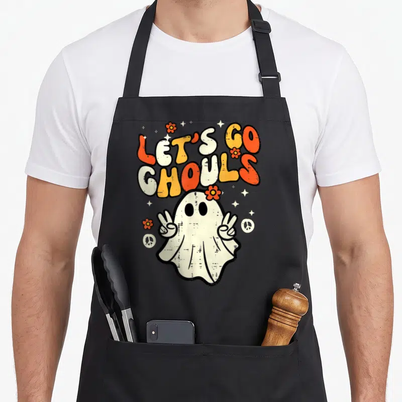 Ghoul halloween apron - Retro ghost making peace signs under stacked orange and white text reading LET'S GO GHOULS — shown on a black cotton canvas apron against a white background