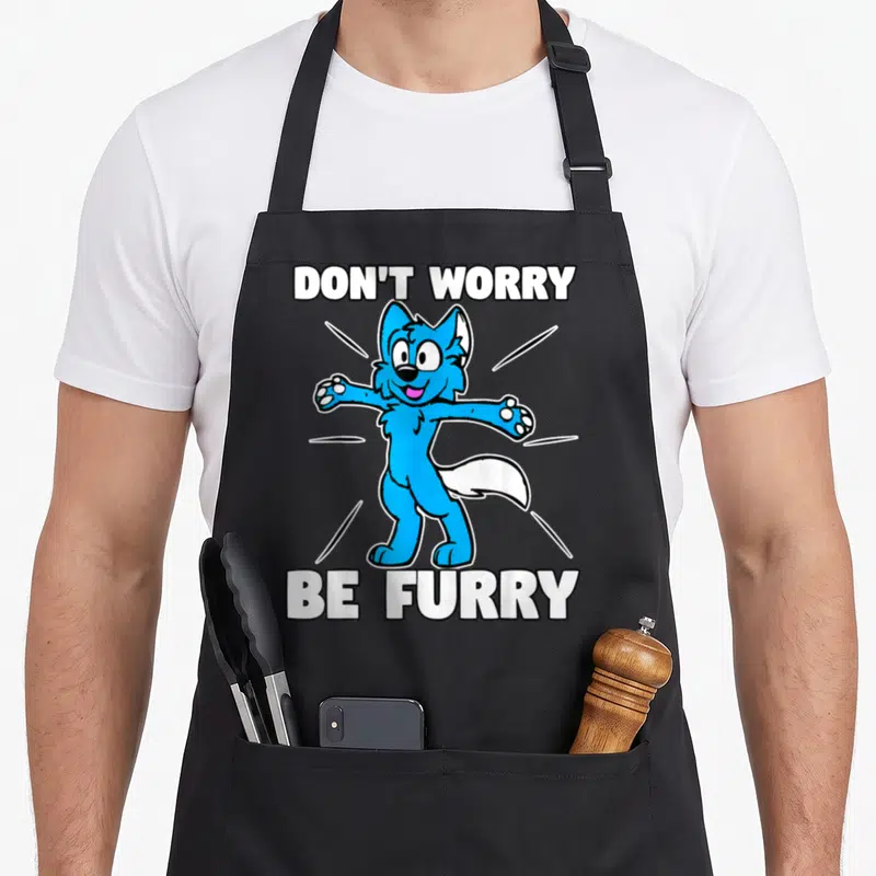 Furry fox aprons - Blue cartoon wolf character between white text DON'T WORRY BE FURRY with radiating lines — shown on a black cotton canvas apron against a white background