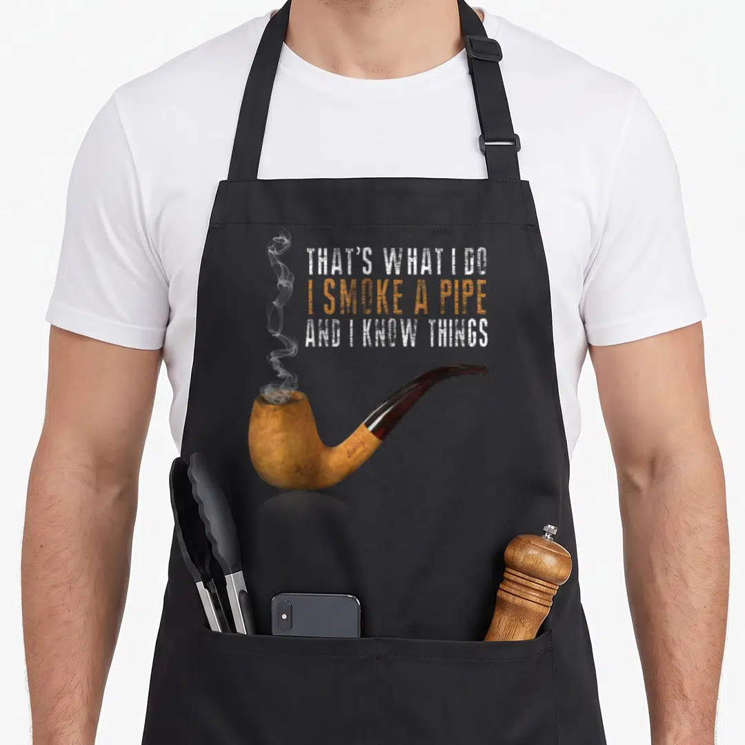 Smoke pipe player apron - Realistic tan pipe with brown stem and stacked text reading THAT'S WHAT I DO I SMOKE A PIPE — shown on a black cotton canvas apron against a white background