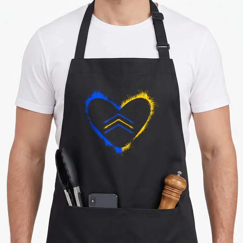 Trisonomy an extra apron - Blue and yellow watercolor heart with two stacked chevrons representing Down Syndrome support — shown on a black cotton canvas apron against a white background