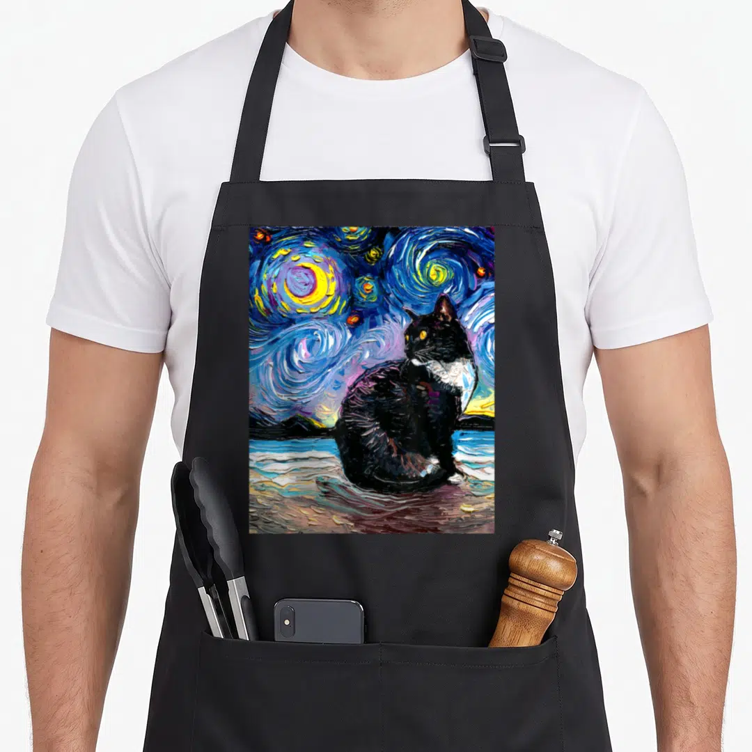 Beach tuxedo apron - Black cat sitting in swirling blue and yellow starry night watercolor painting on black fabric — shown on a black cotton canvas apron against a white background