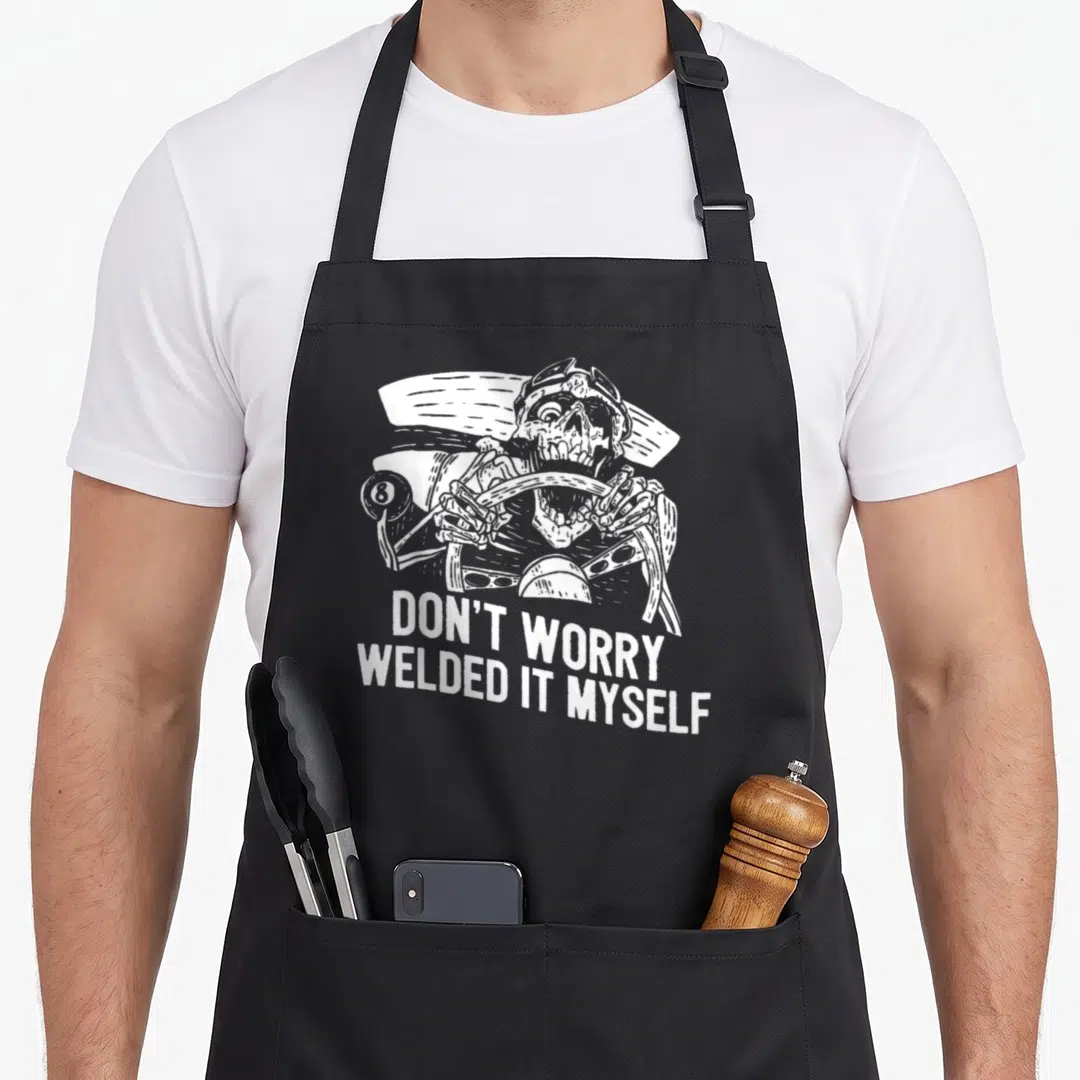 Welder builder apron - White skeleton drawing gripping handlebars above stacked text DON'T WORRY WELDED IT MYSELF — shown on a black cotton canvas apron against a white background