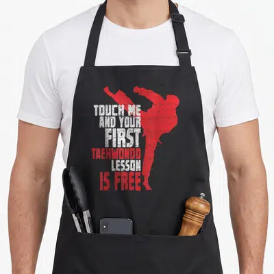 Taekwondo teacher apron - Red kicking silhouette next to stacked text reading TOUCH ME AND YOUR FIRST TAEKWONDO LESSON — shown on a black cotton canvas apron against a white background