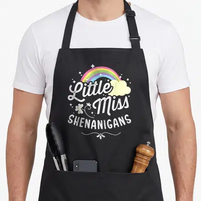 Miss st patrick day aprons - Rainbow cloud Little Miss Shenanigans cartoon graphic with white script and block text — shown on a black cotton canvas apron against a white background