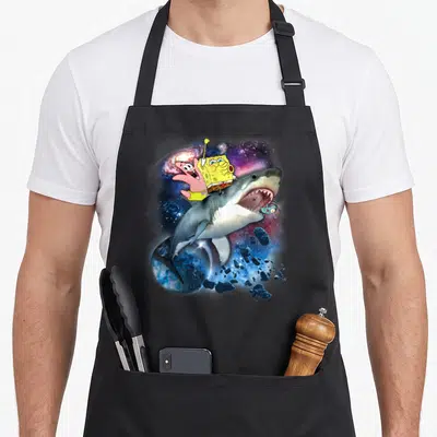Squarepant riding apron - Shark leaping through galaxy with SpongeBob and Patrick riding on back — shown on a black cotton canvas apron against a white background