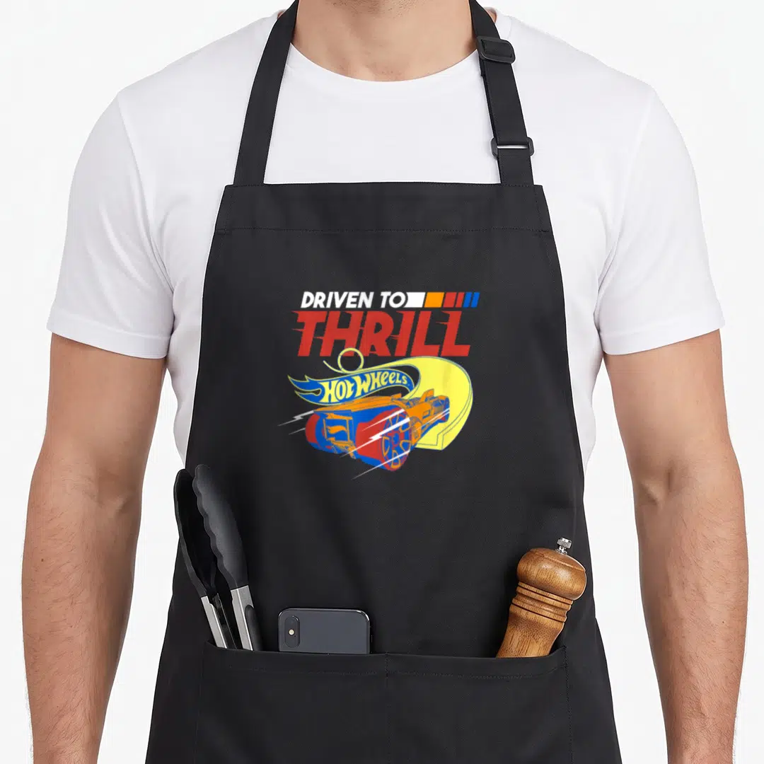 Thrill hot girl apron - DRIVEN TO THRILL text above toy car jumping yellow ramp with flame logo — shown on a black cotton canvas apron against a white background