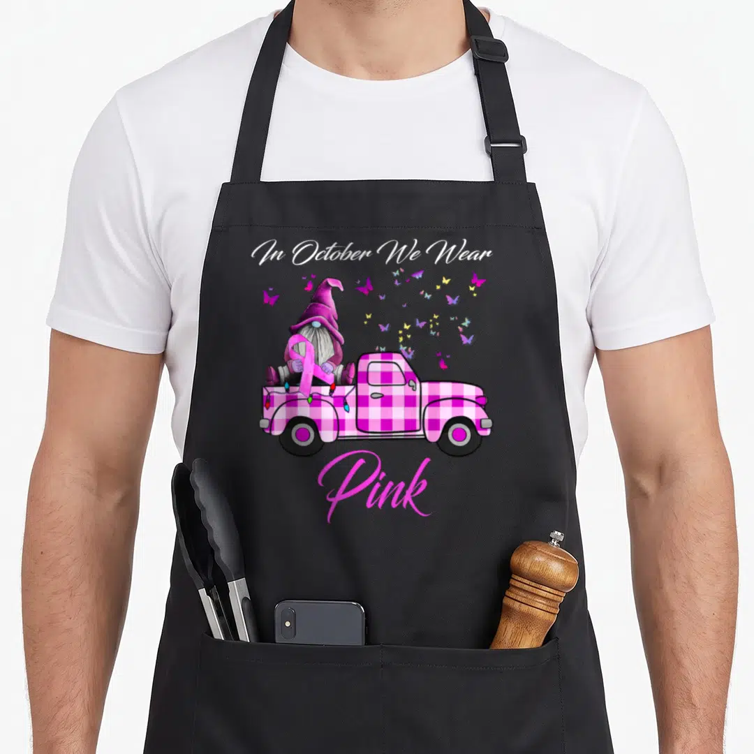 Gnome breast cancer awareness aprons - Pink plaid truck gnome holding ribbon with butterflies and text In October We — shown on a black cotton canvas apron against a white background
