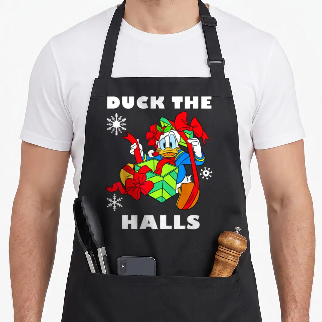 Hall duck apron - Daisy Duck holding green gift box with red ribbons under DUCK THE HALLS text — shown on a black cotton canvas apron against a white background