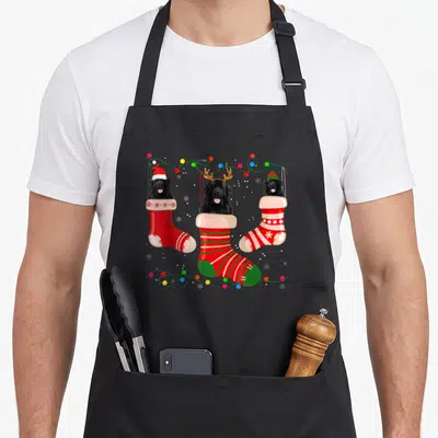 Newfoundland womens christmas aprons - Three black dogs in red and green stockings with Christmas lights and snowflakes — shown on a black cotton canvas apron against a white background