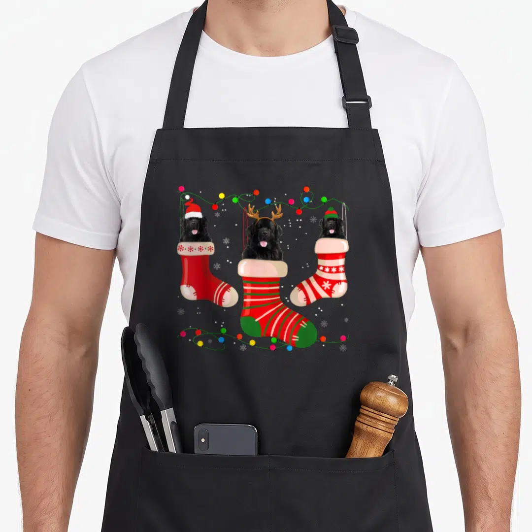 Newfoundland womens christmas aprons - Three black dogs in red and green stockings with Christmas lights and snowflakes — shown on a black cotton canvas apron against a white background
