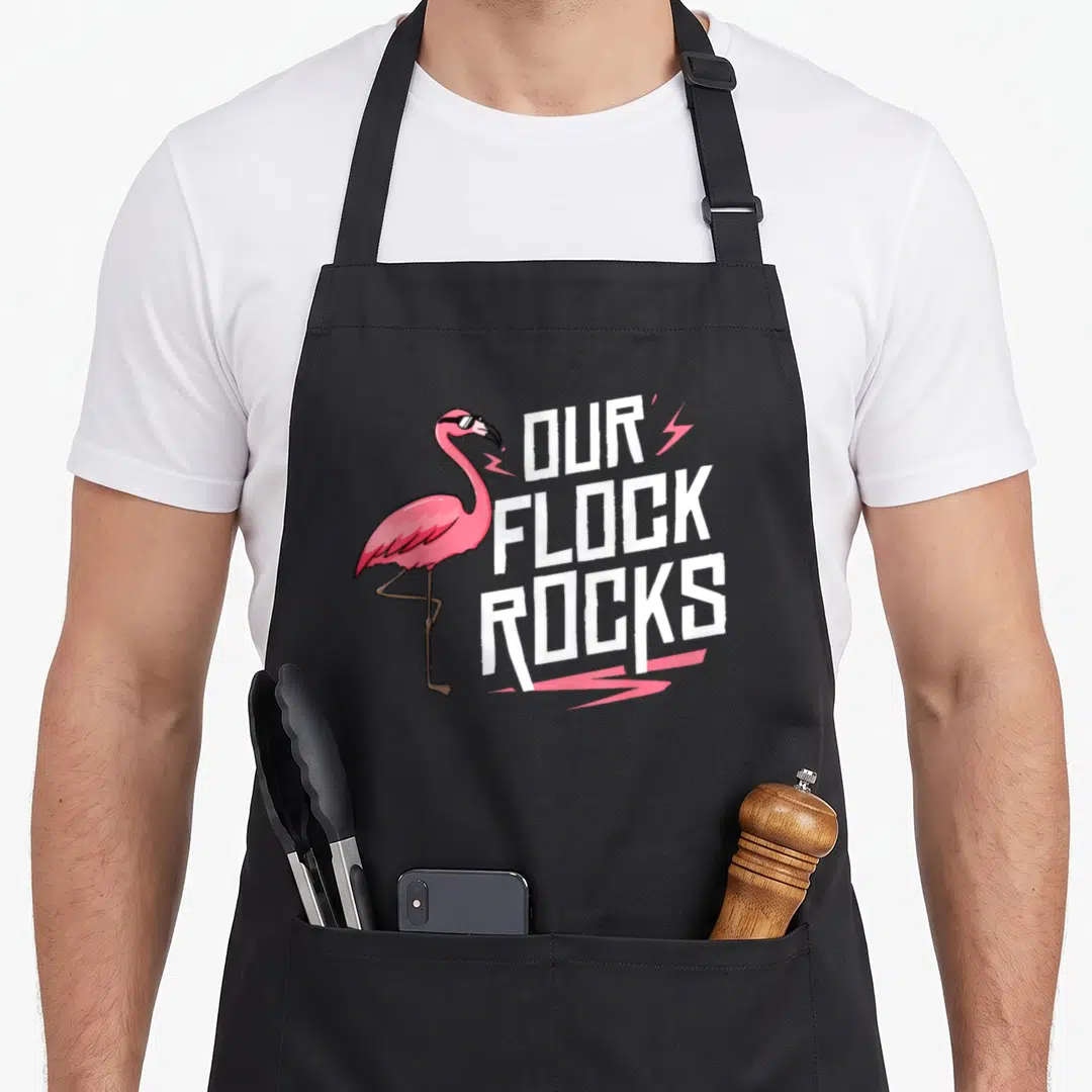 Our pink flamingo apron - Cartoon flamingo wearing sunglasses next to white text and pink lightning bolts — shown on a black cotton canvas apron against a white background