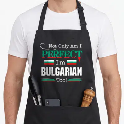 Perfect country apron - Text design Not Only Am I Perfect I'm Bulgarian Too with small Bulgarian flags — shown on a black cotton canvas apron against a white background